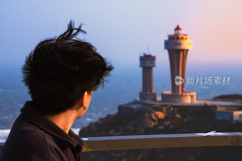 男子眺望远方灯塔的海边风景图