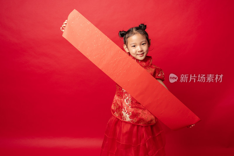 红色背景前穿旗袍拿空白春联纸的中国女孩