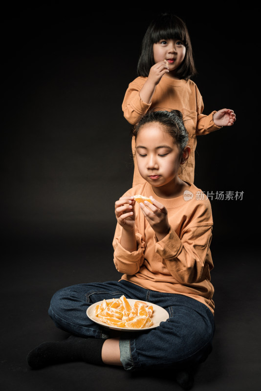 坐在黑背景前吃水果的两个亚裔女孩