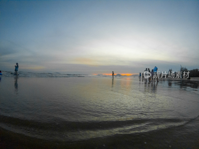日落时海滩上的人们在天空的映衬下剪影