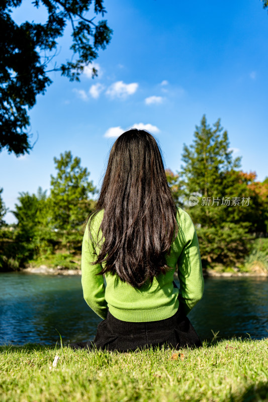 背对着天空坐在湖边的女人的后视图