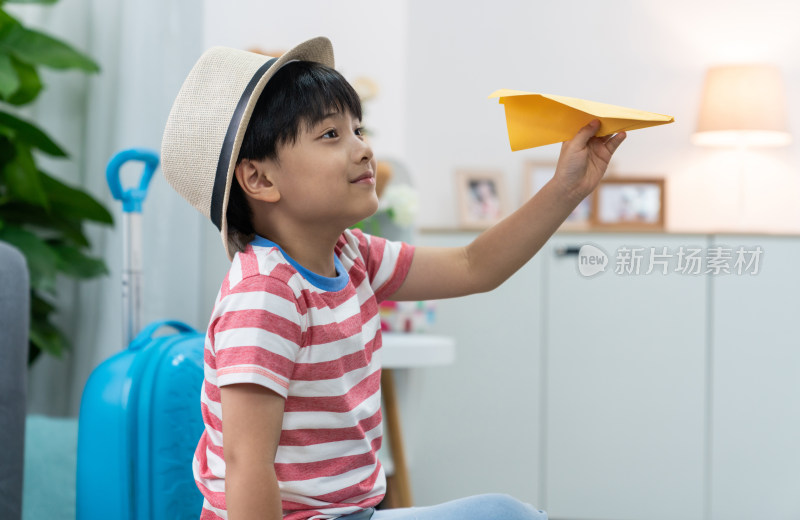 快乐的小男孩拿着纸飞机坐在行李箱上