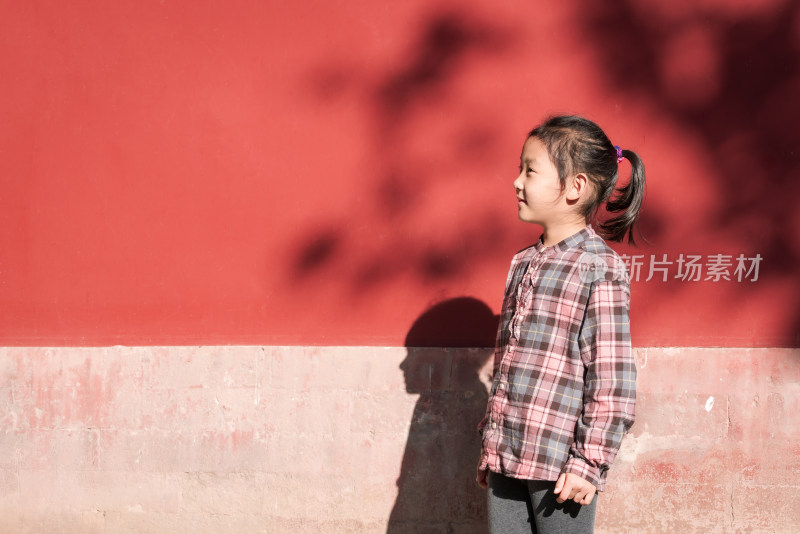 在公园红色围墙下走过的中国女孩