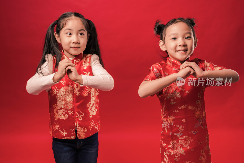 两个站在红色背景前穿唐装作揖的中国女孩