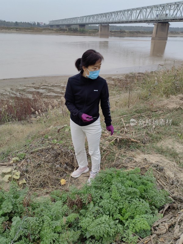 戴口罩的女士站在河边的土地上