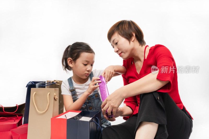 坐在白色背景前拆开礼物的中国籍母女