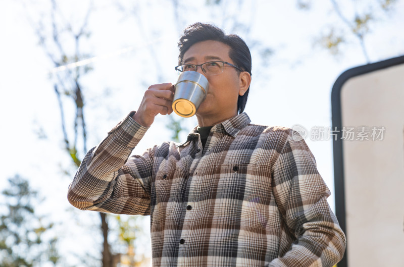 一个老年男人站在房车前喝咖啡