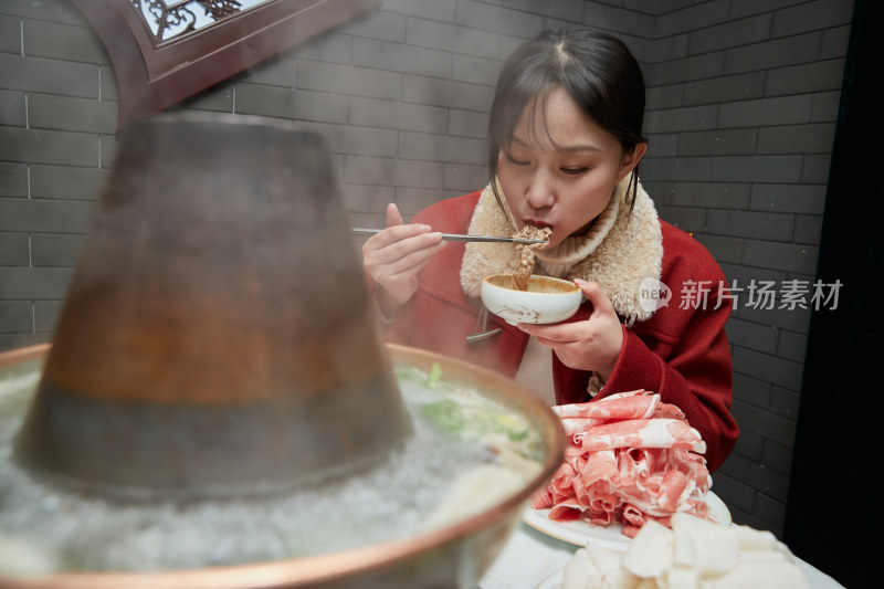 在饭店吃传统铜锅涮肉的亚洲少女