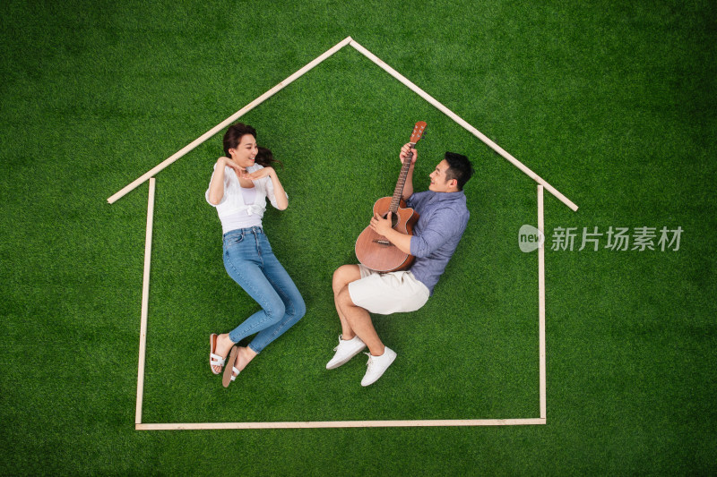 青年伴侣躺在草地上的房子轮廓里唱歌跳舞