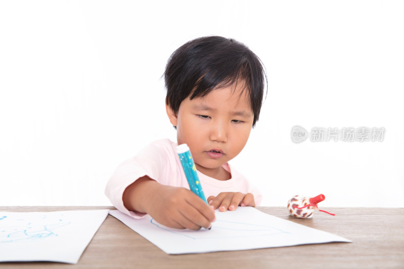 白背景前趴在桌子上认真画画的小女孩