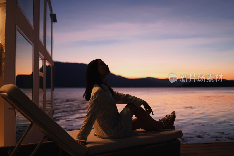 夕阳下坐在海边的女人的侧视图