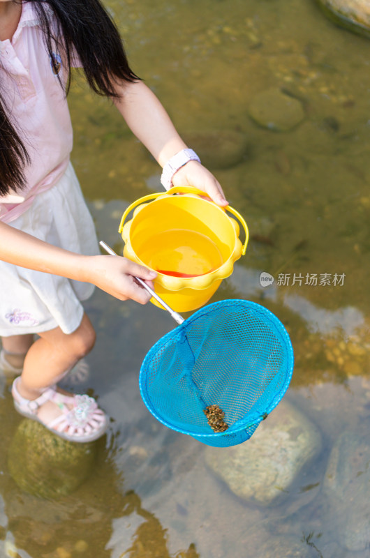 小女孩在水中手持网兜和水桶的场景