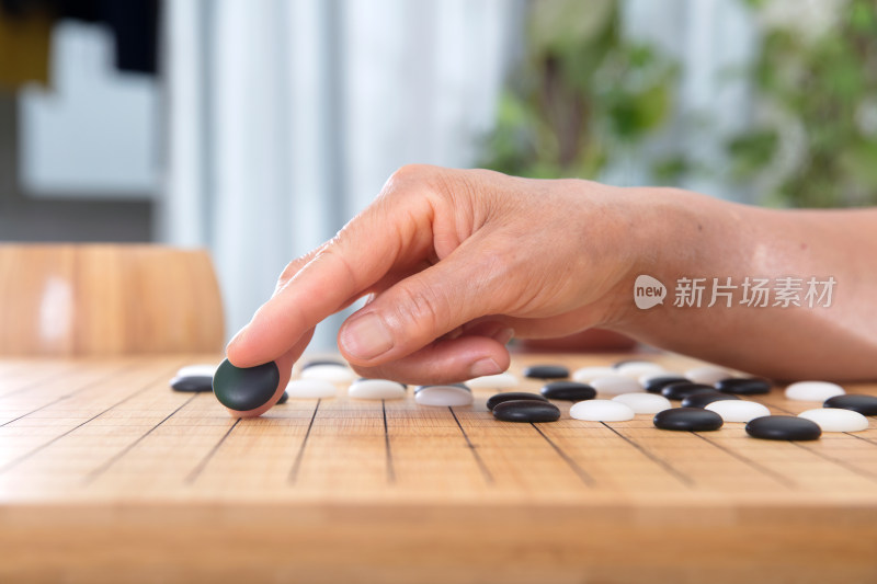 一只老人的手指夹着一枚黑色棋子下棋