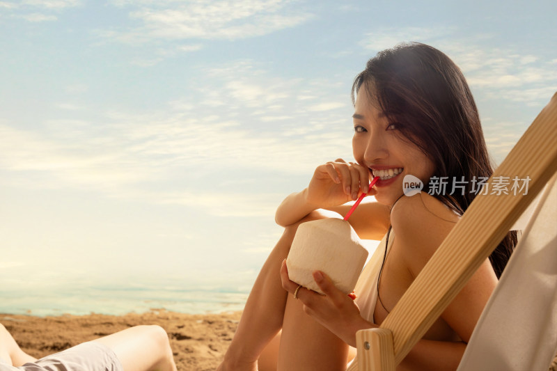 青年女孩在沙滩上喝椰汁