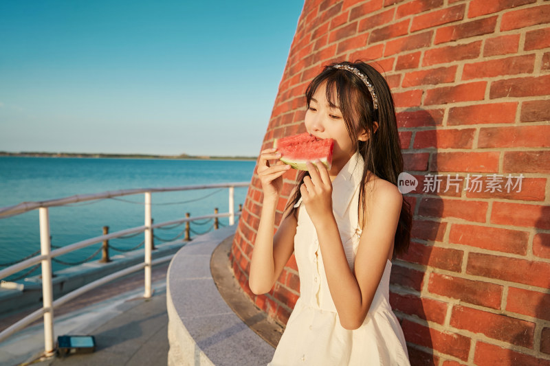 盛夏夕阳湖边码头灯塔上吃西瓜的少女