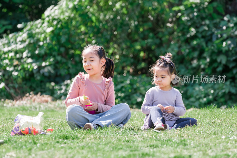 秋天午后两个坐在草坪上玩气球的女孩