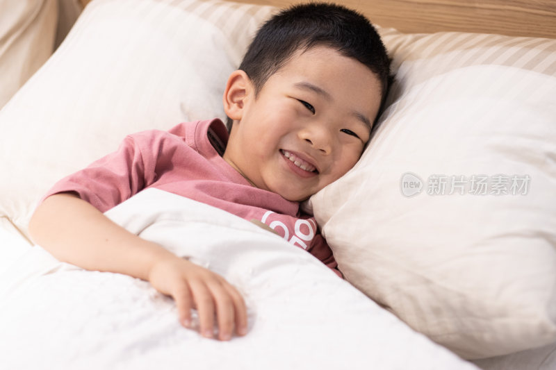 一个小男孩躺在舒适的床上盖着被子