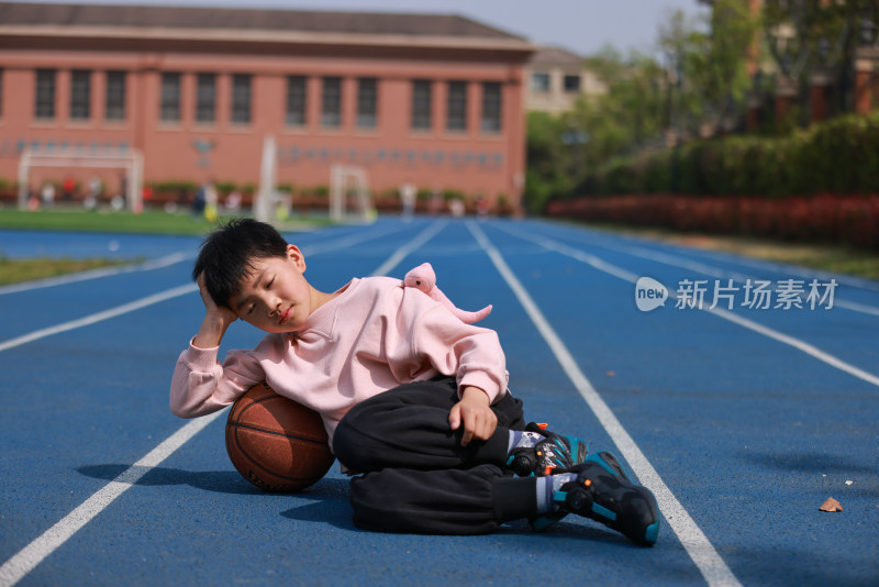 可爱的男孩靠在篮球上休息