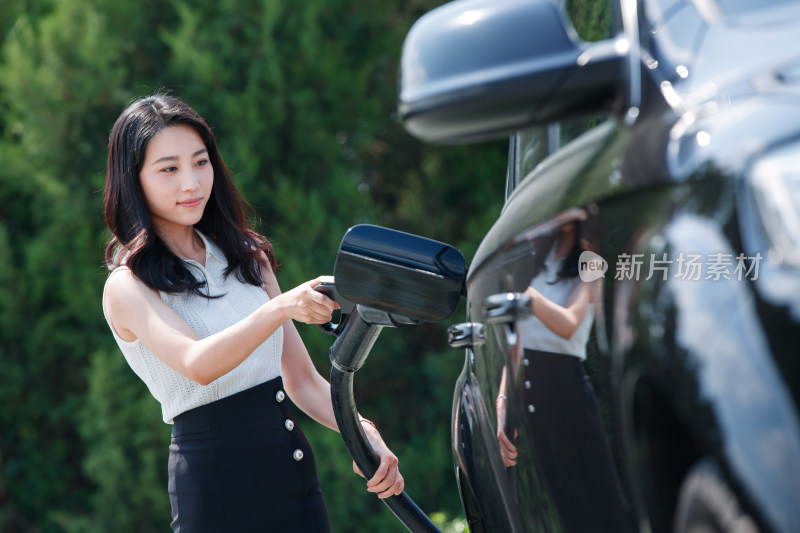 青年女人拿着充电枪准备给汽车充电