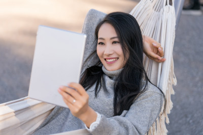 年轻女子躺在吊床上使用平板电脑