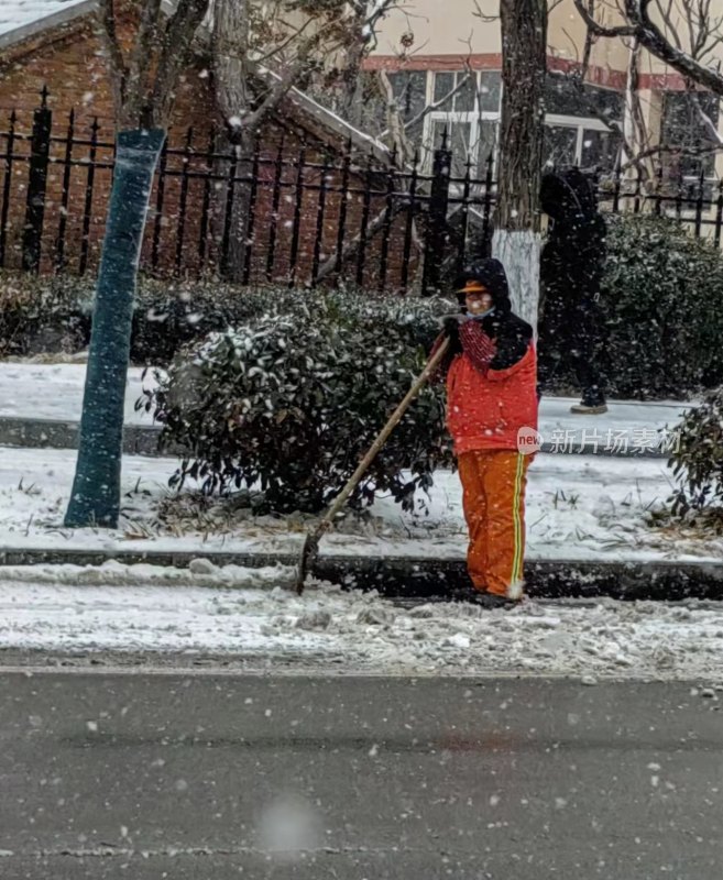 穿红衣的环卫工人在雪中清扫街道