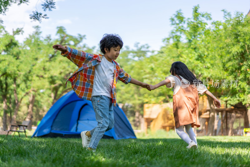 两个孩子在草地上手拉手开心转圈做游戏