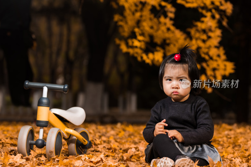 深秋坐在公园落满黄叶的草地上玩耍的女孩