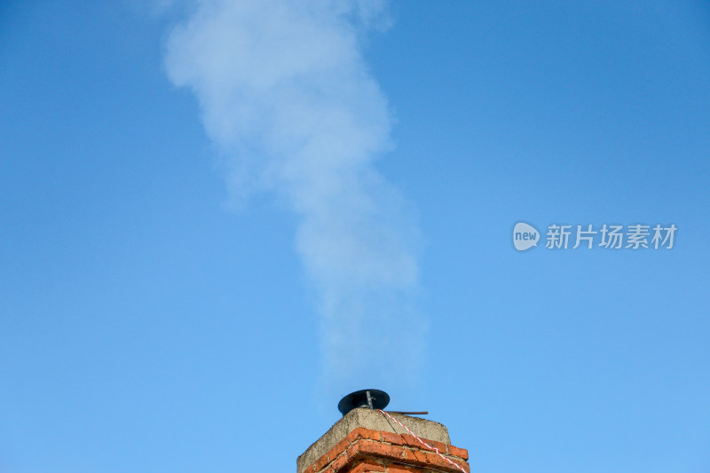 蓝天背景下烟囱冒出袅袅烟雾的景象